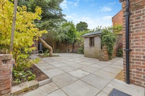 A paved patio area with a brick wall, a wooden shed, and a tree with yellow leaves. - 2 Bed in Wells-next-the-Sea (oc-c29565) (Wells-next-the-Sea)
