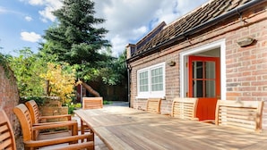 Une terrasse en bois avec une table et des chaises, entourée d’un mur de briques et d’une porte rouge.