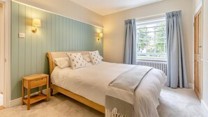 Une chambre à coucher avec un lit, une table de chevet, une lampe, une fenêtre et des rideaux.