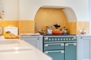 A kitchen with a stove, a pot on the stove, and a yellow-tiled backsplash. - 2 Bed in Wells-next-the-Sea (oc-c29565) (Wells-next-the-Sea)