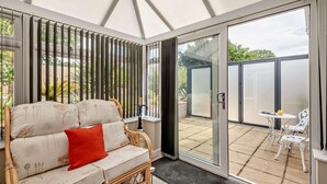 En overdækket patio med en fletsofa, en rød pude og et bord med et glas.