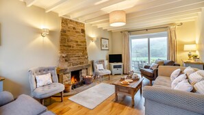 A cozy living room with a stone fireplace, comfortable seating, a flat-screen TV, and a large window with curtains. - 3 Bed in Horsehouse (oc-e29610) (Horsehouse)