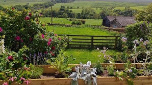 A rural landscape with a wooden fence, a small barn, and a variety of flowering plants in the foreground. - 3 Bed in Horsehouse (oc-e29610) (Horsehouse)