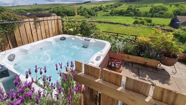 A hot tub on a wooden deck with a view of green fields and a cloudy sky. - 3 Bed in Horsehouse (oc-e29610) (Horsehouse)