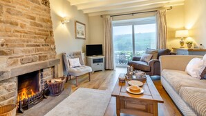 A cozy living room with a stone fireplace, comfortable seating, a television, and a large window offering a scenic view. - 3 Bed in Horsehouse (oc-e29610) (Horsehouse)