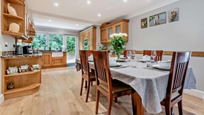 A spacious dining area with wooden furniture, a table set for four, and a view of the kitchen in the background.