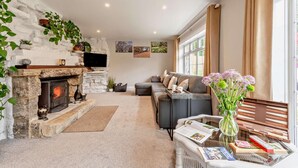 A cozy living room with a stone fireplace, a sofa, a coffee table with magazines, and a window with curtains.