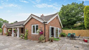 A brick house with a tiled roof, a porch with hanging flower baskets, and a stone patio.