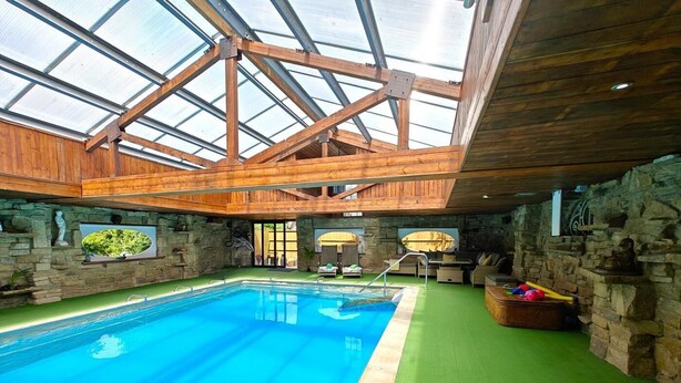 An indoor swimming pool with a wooden ceiling and stone walls.