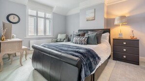 Quarto com cama, mesa de cabeceira, luminária, cadeira e janela com persianas.