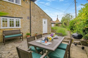 A stone house with a patio area featuring a wooden table, chairs, a bench, and a barbecue grill. - 3 Bed in Powerstock (oc-r29646) (Powerstock)