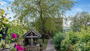 En stenväggsbrunn med en träkonstruktion, omgiven av frodig grönska och en stenmur.