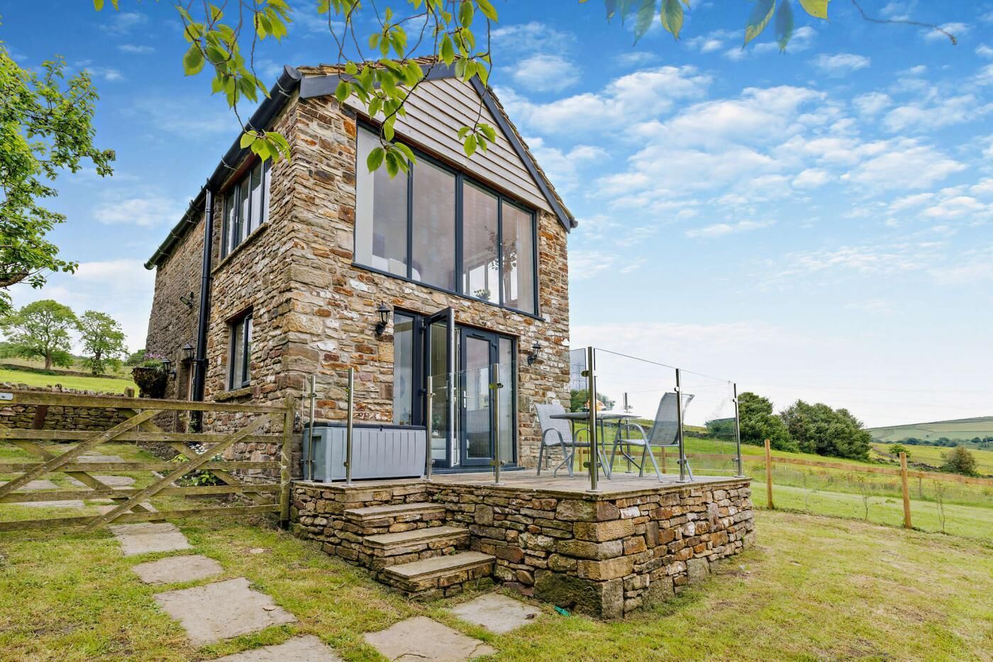 A stone house with a large glass window, a wooden deck, and a view of the countryside.