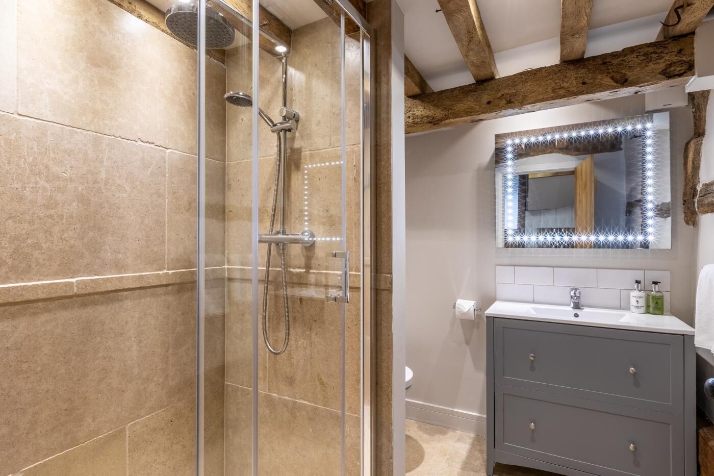 Un baño con cabina de ducha de vidrio, tocador con espejo y viga de madera en el techo.