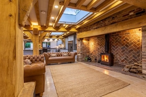 A cozy living area with a fireplace, wooden beams, and a skylight. - 5 Bed in Frampton On Severn (oc-d29489) (Frampton on Severn)