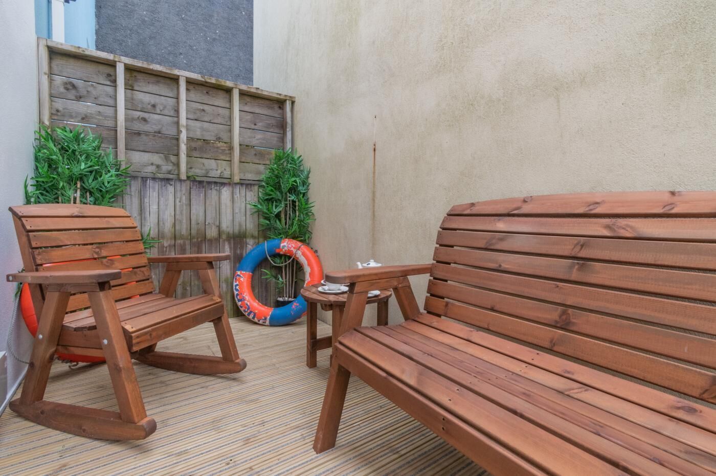 A wooden outdoor seating area with a bench and chairs, a small table, and a life ring.