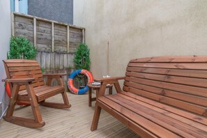 A wooden outdoor seating area with a bench and chairs, a small table, and a life ring. - 3 Bed in Tenby (oc-m29588) (Tenby)
