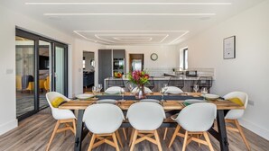 Un comedor moderno con una mesa larga, sillas blancas y un jarrón central con flores.