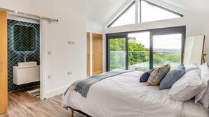 Un dormitorio con una cama grande, un tragaluz, un balcón con vistas y un baño moderno con un revestimiento de pared en patrón espiga.