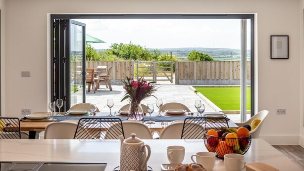 Un comedor con una mesa dispuesta para cuatro, vistas al exterior y un frutero sobre la mesa.