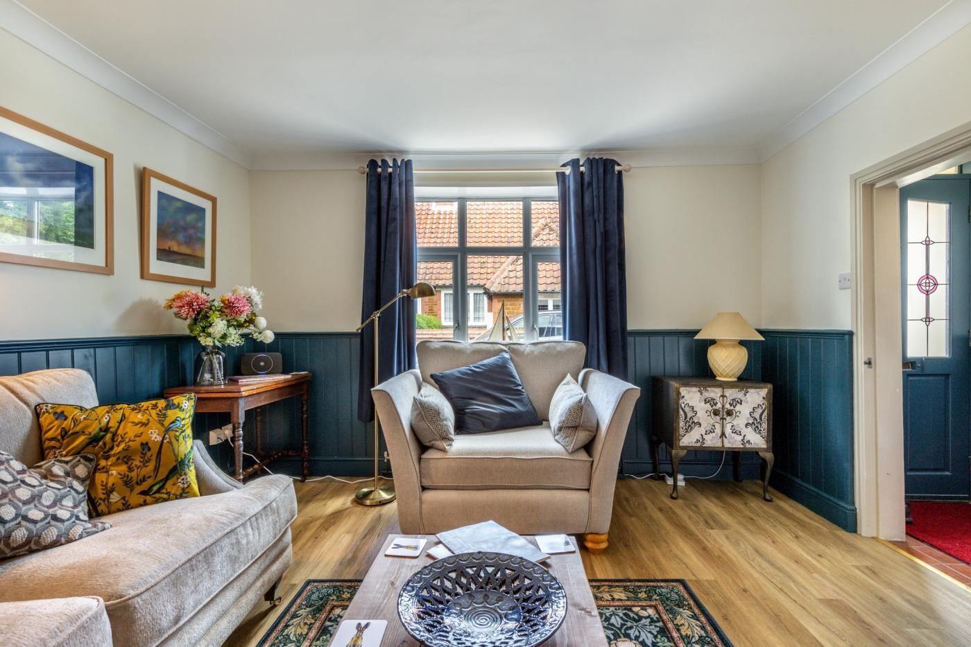 A cozy living room with a sofa, a side table with a lamp, and a window with curtains.