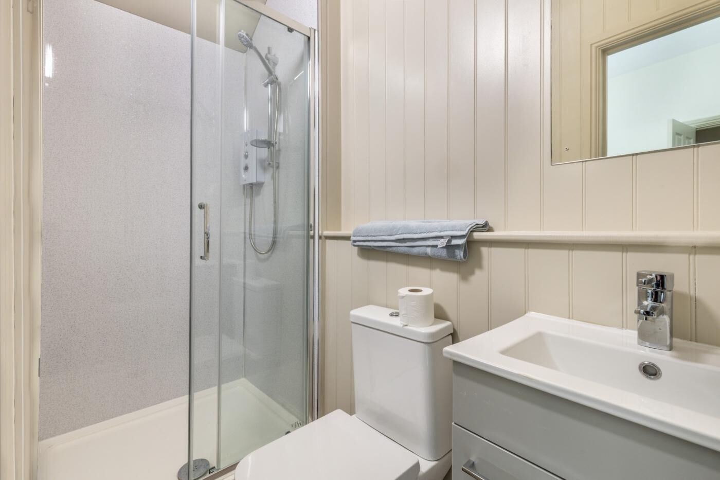 Et moderne badeværelse med en glasafskærmet brusekabine, toilet og et spejl over vasken.