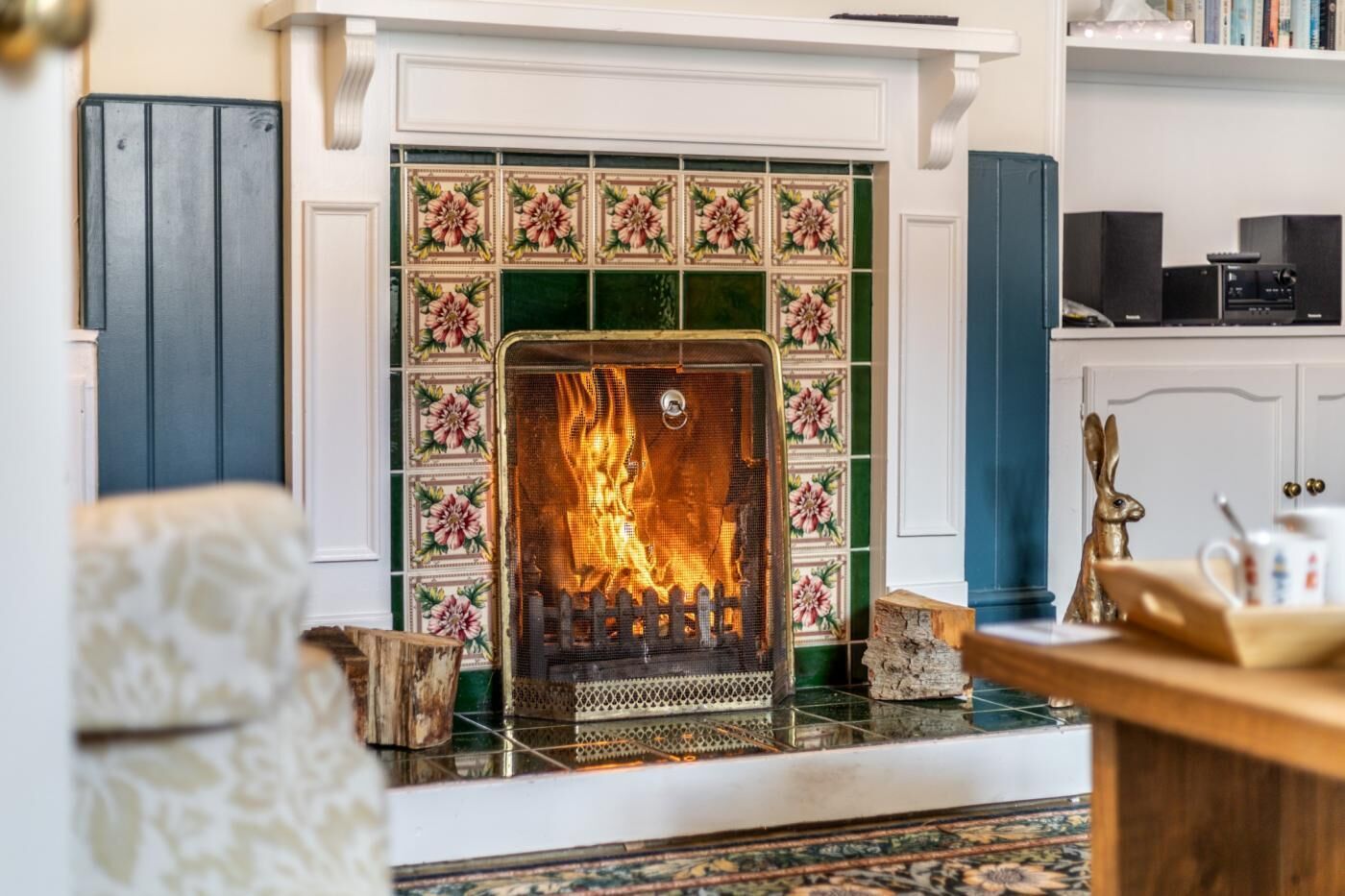 A fireplace with a fire, surrounded by patterned tiles and a mantelpiece.