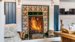 A fireplace with a fire, surrounded by patterned tiles and a mantelpiece. - 2 Bed in Snettisham (oc-t29559) (Snettisham)