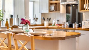A modern kitchen with a central island, wooden chairs, and a dining table set for four. - 2 Bed in Snettisham (oc-t29559) (Snettisham)
