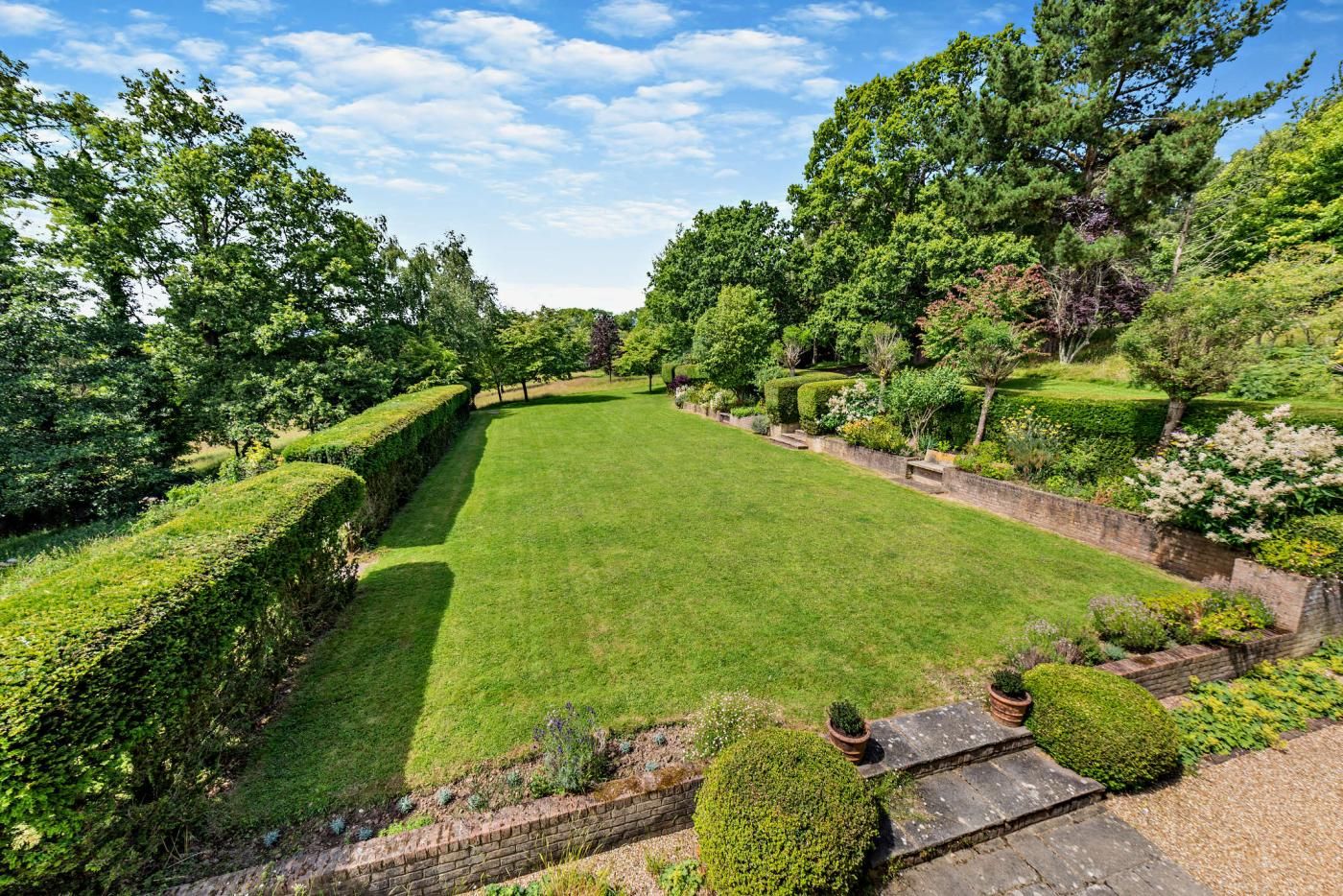 A well-maintained garden with a central lawn, bordered by hedges and various shrubs.