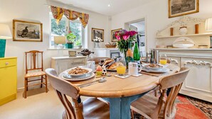 Un coin repas avec une table ronde mise pour le petit-déjeuner, comprenant des assiettes remplies de nourriture, une cafetière et un vase avec des fleurs.