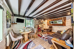 Un intérieur chaleureux avec un mur en pierre, des poutres apparentes, une cheminée, des fauteuils en cuir et un coin repas.