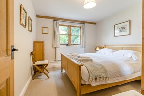 Une chambre à coucher avec un lit en bois, une chaise, une fenêtre avec des rideaux et des tableaux encadrés accrochés au mur.