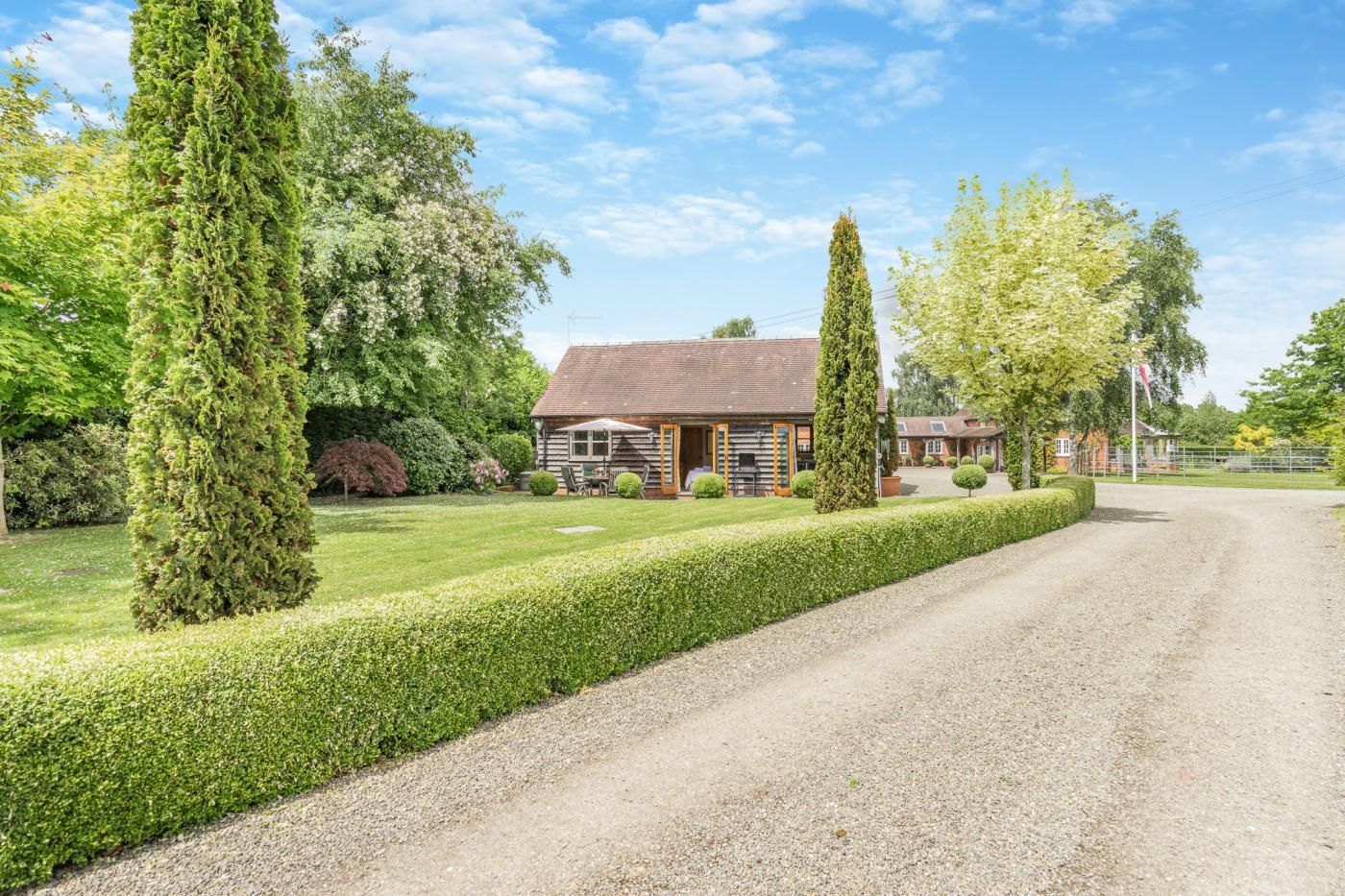 A rural property with a gravel driveway leading to a stone building with a tiled roof.