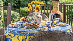 Ein Frühstückstisch im Freien mit einem Korbstuhl, einem Korb, einer Blumenvase mit Sonnenblumen, einer Kaffeekanne und einem Terrakottatopf.