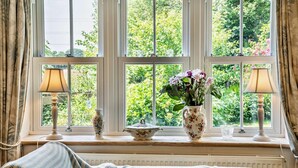 Ein gemütliches Zimmer mit Fenster, einer Couch, zwei Lampen, einer Blumenvase und einer dekorativen Schale auf der Fensterbank.