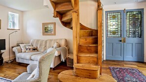 Ein gemütliches Wohnzimmer mit einer Holz-Wendeltreppe, einer Couch, einem Sessel, einem Fernseher und einer Tür mit Buntglasfenstern.