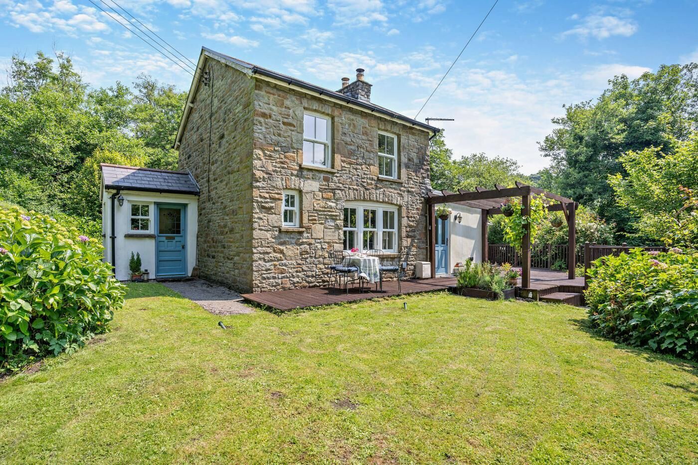 A stone house with a small garden, a patio with outdoor seating, and a wooden pergola.