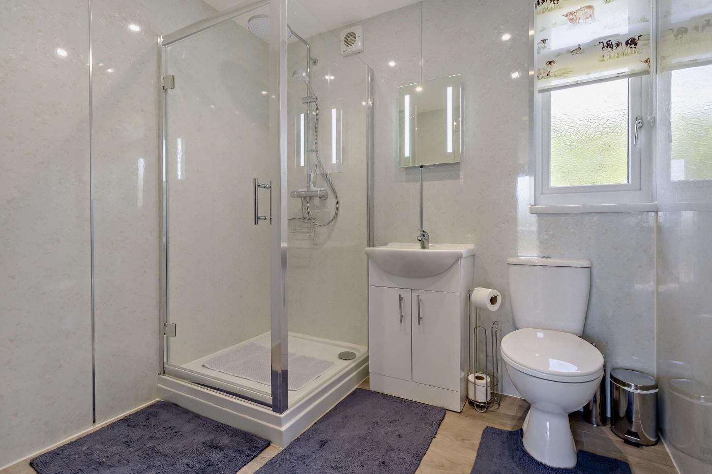 Un baño moderno con ducha envuelta en vidrio, un lavamanos blanco y un inodoro.