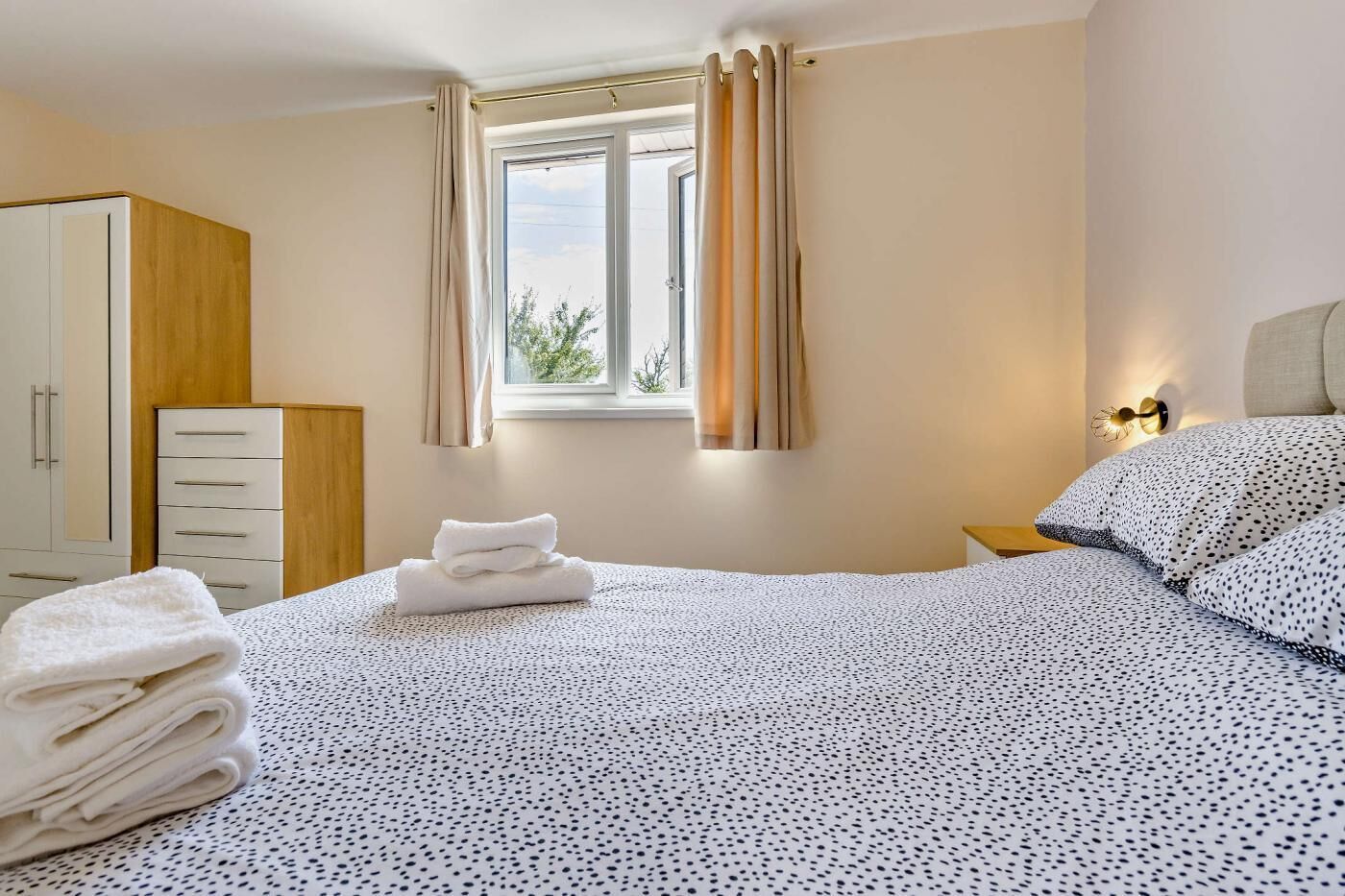 A bedroom with a bed, a wardrobe, a window with curtains, and a nightstand with a lamp.