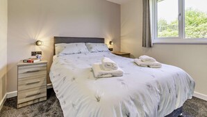 Une chambre à coucher comprenant un lit, des tables de chevet, une commode, une fenêtre et une vue sur la verdure à l’extérieur.