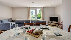 Un coin repas avec une table dressée pour quatre personnes, un canapé et un téléviseur, le tout dans une pièce offrant une vue sur la verdure.
