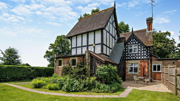 A Tudor-style house with a steeply pitched roof, a brick chimney, and a well-maintained garden with a pathway leading to the entrance. - 1 Bed in Tollard Royal (oc-l29639) (Tollard Royal)