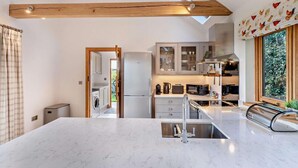 A modern kitchen with a marble countertop, wooden beams, and a view of the garden through a large window. - 1 Bed in Stone (oc-t29685) (Stone in Oxney)