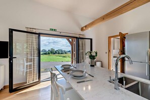 A modern kitchen with a large window, a dining area with a table set for two, and a view of a green landscape. - 1 Bed in Stone (oc-t29685) (Stone in Oxney)