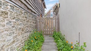 Ein schmaler Steinweg, begrenzt von einem Holzzaun und einem Gebäude mit einem geneigten Dach.