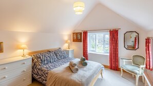 Ein Schlafzimmer mit Bett, Nachttischen, einem Sessel, einem Fenster mit Vorhängen und einer Deckenleuchte.