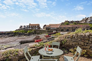 Una zona costiera con edifici in pietra, una spiaggia rocciosa e un tavolo con sedie e un piatto di cibo.
