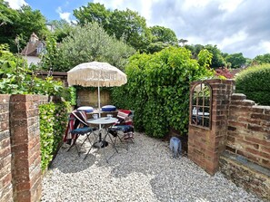 Un patio con mesa y sillas, rodeado por un muro de ladrillo y vegetación.