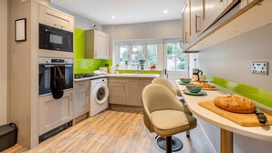 A modern kitchen with built-in appliances, a washing machine, and a dining area with a chair and a cutting board. - 1 Bed in Lewes (oc-n29713) (Lewes)